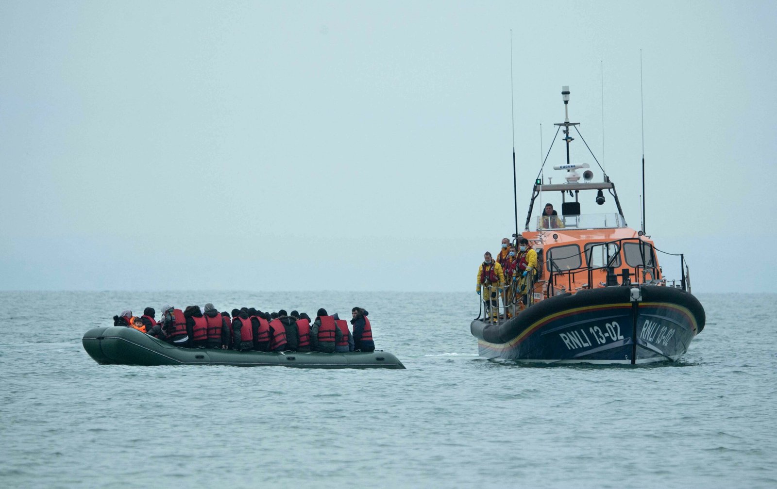TOPSHOT - Migrants are helped by RNLI (Royal National Lifeboat Institution) lifeboat before being taken to a beach in Dungeness, on the south-east coast of England, on November 24, 2021, after crossing the English Channel. - The past three years have seen a significant rise in attempted Channel crossings by migrants, despite warnings of the dangers in the busy shipping lane between northern France and southern England, which is subject to strong currents and low temperatures. (Photo by Ben STANSALL / AFP)